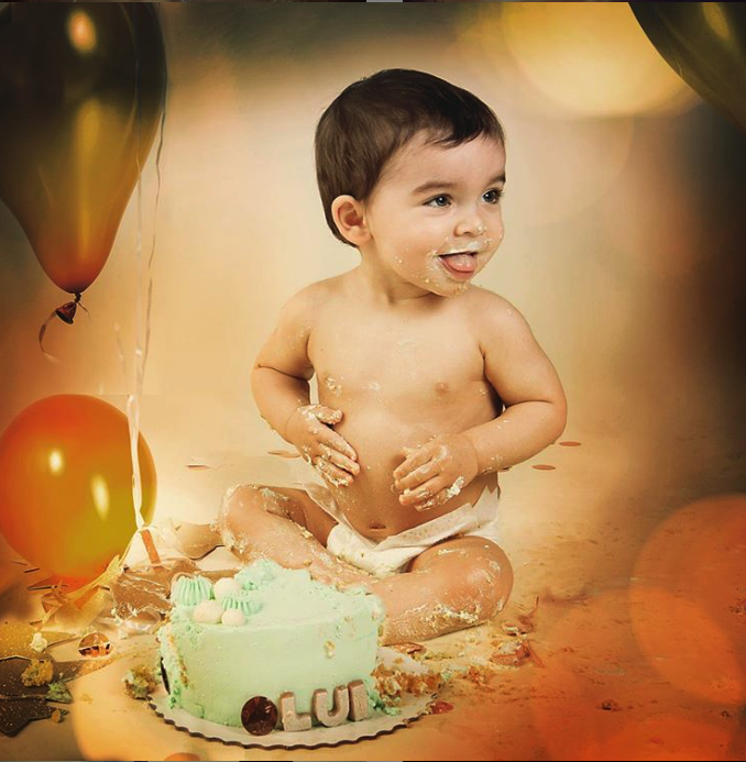 Bebé de 1 año en un estudio fotográfico con un pastel y globos, cumpleaños  de un niño de 1 año, el bebé come pastel